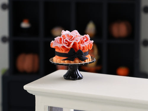 Decorative cake with pink frosting and black ribbons on a stand against a blurred background